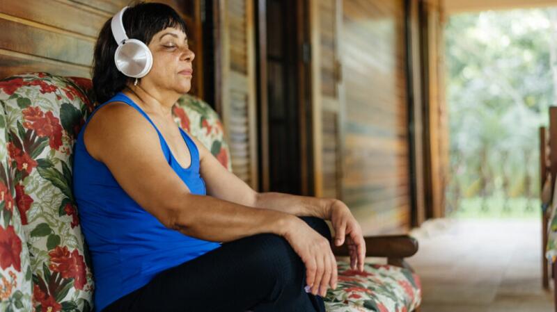 person with eyes closed wearing workout clothes and headphones sitting cross-legged on a bench