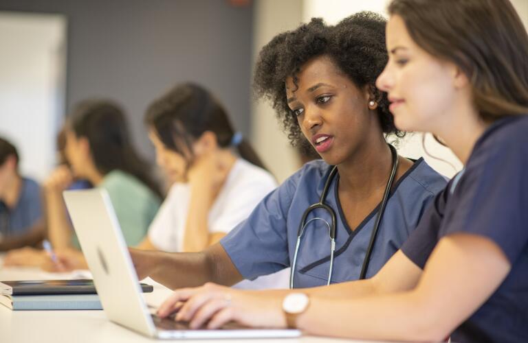 two female medical students in classroom looking at laptop