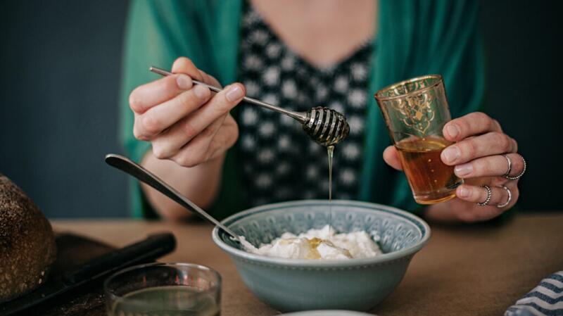 a person is pouring honey over yogurt, a great food for gut health