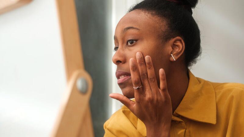 Person looking in mirror examining face with hand on cheek