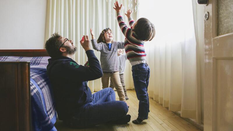 Father sitting on floor blowing bubbles with young children reaching up