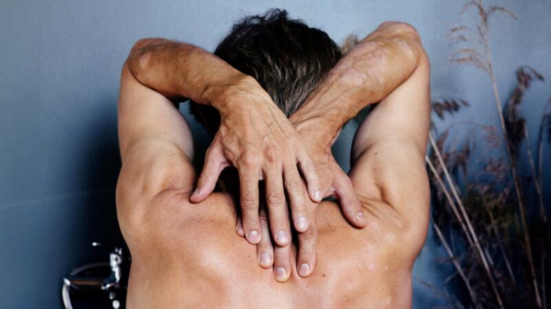 A person feels the skin on the upper back with both hands.