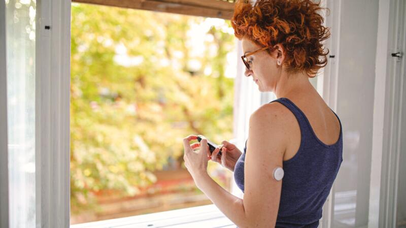 adult female wearing a patch-style blood glucose monitor