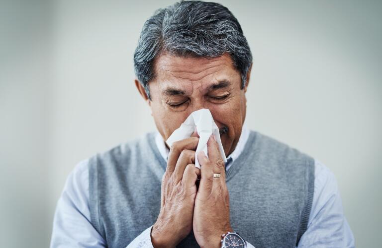senior male blowing nose with tissue