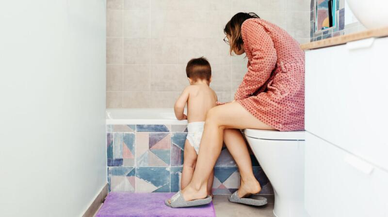 Mother and older baby or toddler standing next to bathtub in bathroom