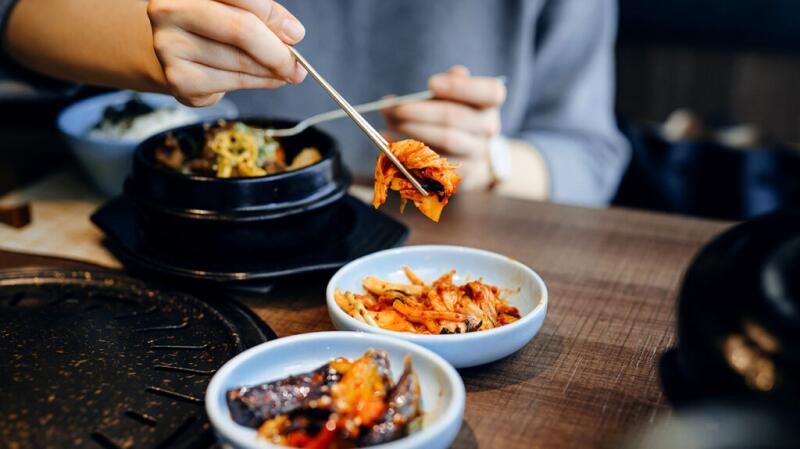 A person picks up some kimchi from a bowl using chopsticks.