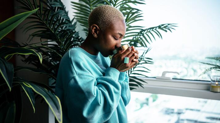 Woman stands and drinks hot tea from a mug with closed eyes
