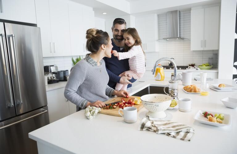 Young Caucasian girl with parents in kitchen as mother chops strawberries