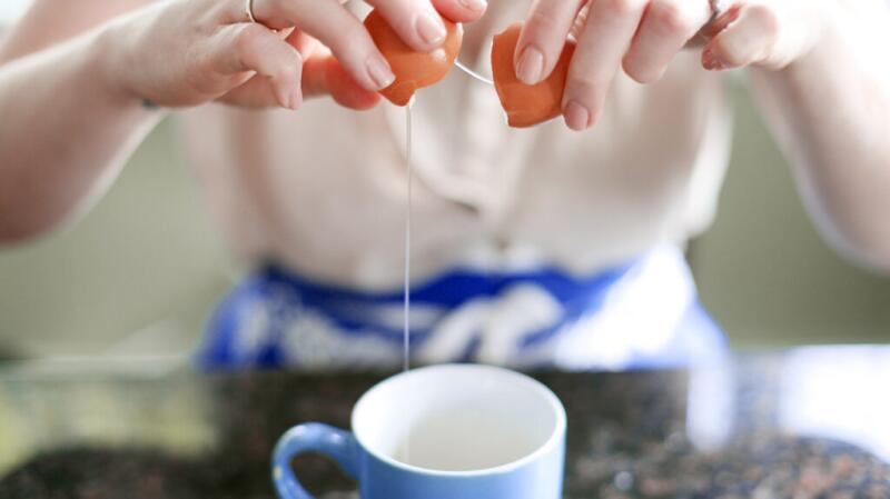 Someone cracks open an egg and lets the egg whites fall into a cup.