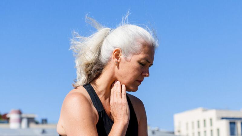 A woman feeling the front of her neck