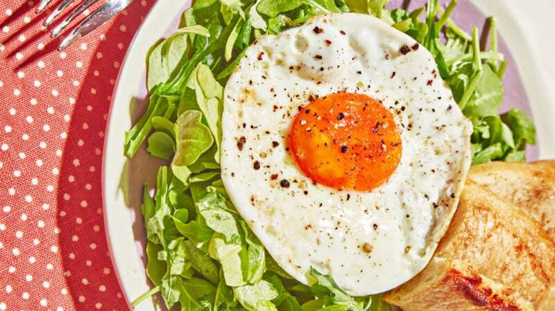 A fried egg sits on top of a bowl of salad, on a spotted table cloth.