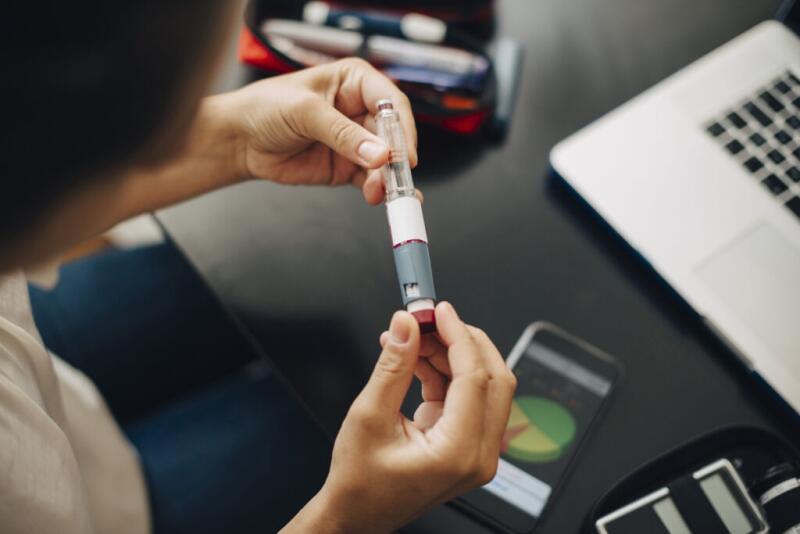 Cropped image of businesswoman holding injection pen while sitting at office desk