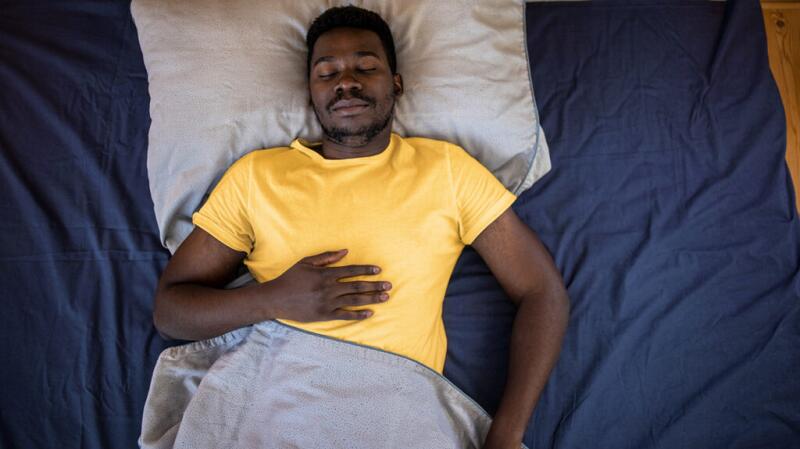 A man is lying in bed with his hand on his stomach.