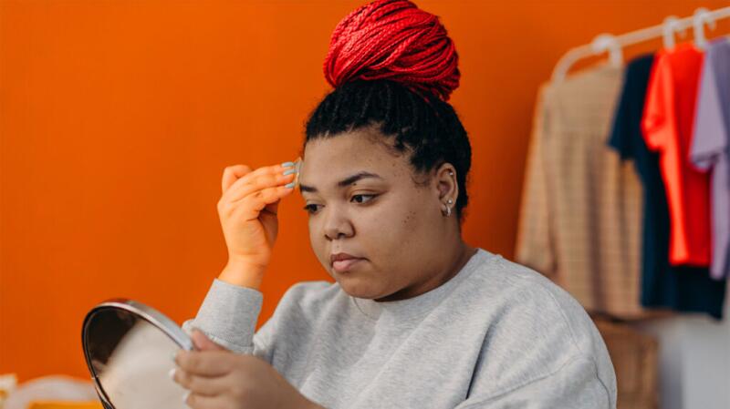 Woman putting on makeup looking in handheld mirror