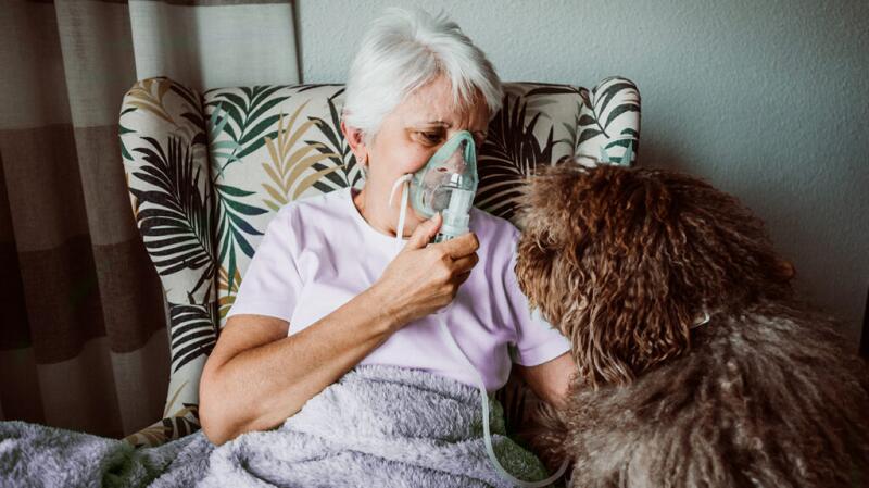 Senior woman wearing oxygen mask petting her dog in chair