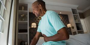 Older African American man with stomach pain sitting on side of bed
