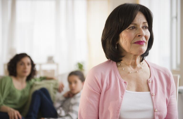 Older Hispanic woman looking concerned with daughter and granddaughter in background