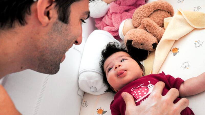 Young infant lying on back sticking tongue out at smiling father