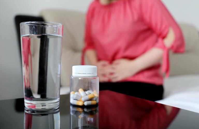 Woman suffering from pain in abdomen with glass of water and bottle of pills in foreground