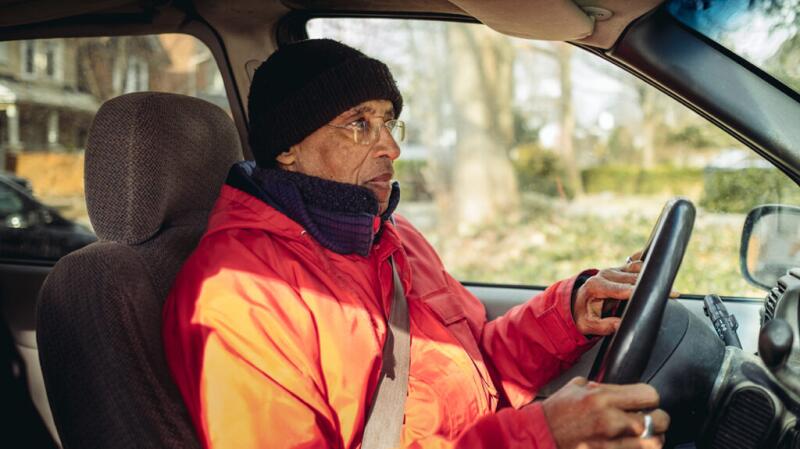 An older adult sits at the steering wheel of a car.
