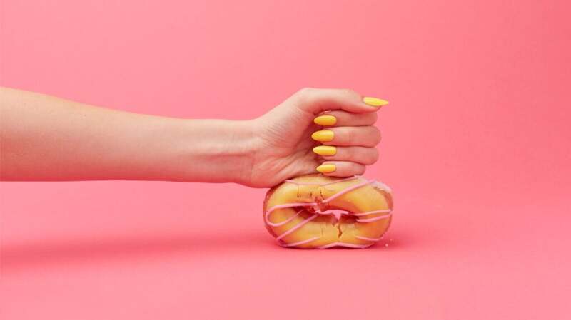A person's fist squashes a ring donut.
