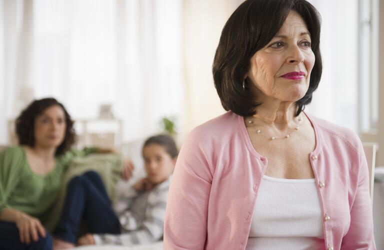 Older women looking into distance with concerned family members in background