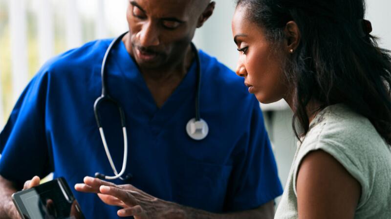 Male doctor showing image to female patient on tablet