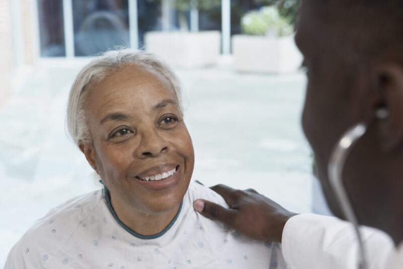 Senior African woman smiling at African doctor in hospital