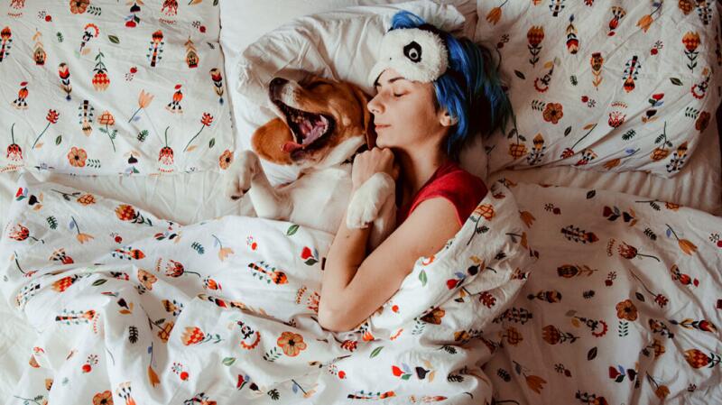 Female lying bed with a yawning dog