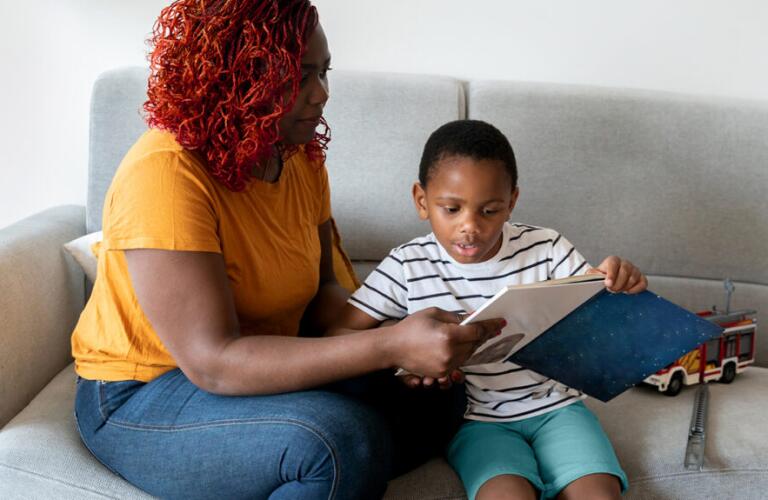 Mother and young son reading a book together on a couch