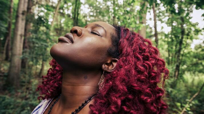 A woman closes her eyes in a forest. 