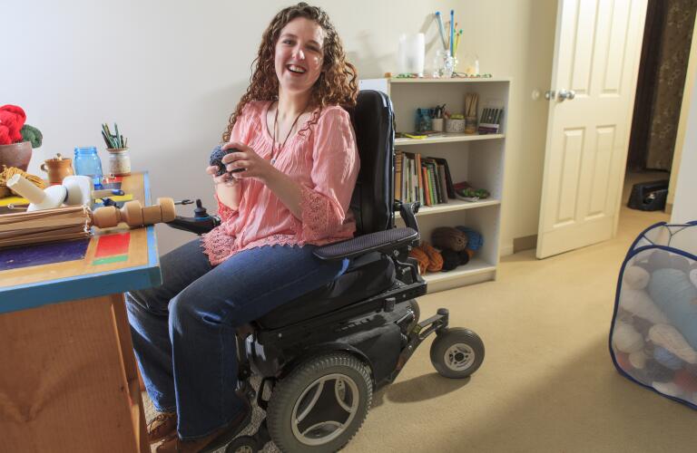 Young woman with muscular dystrophy in wheelchair at desk in bedroom