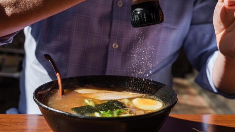 Image of person salting a bowl of ramen