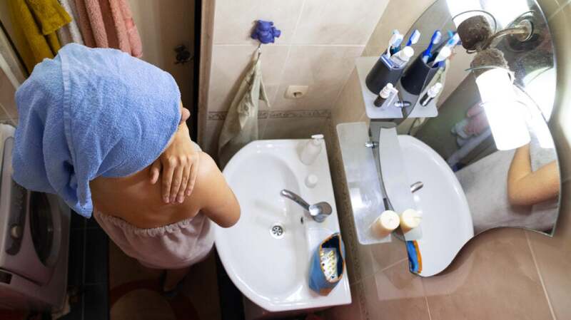 A person is applying moisturizer after showering.