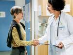 A doctor shakes hands with a patient in a medical office hallway.