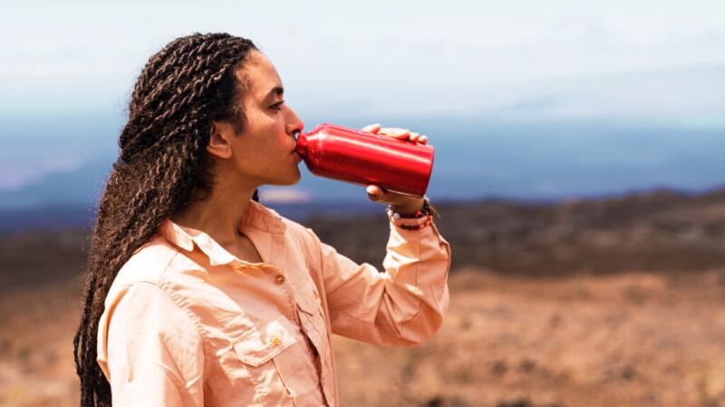Woman is drinking water from a water bottle while outside.