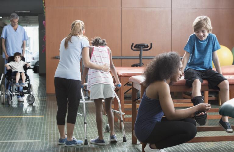 physical therapists helping children, one with a medical walker (walking aid)
