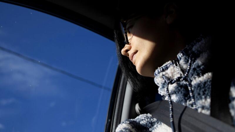 A person looks out a car window with direct sunlight hitting their face.