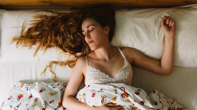 a woman is asleep on her back in a white bed