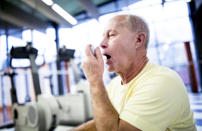 senior man using inhaler while exercising at gym