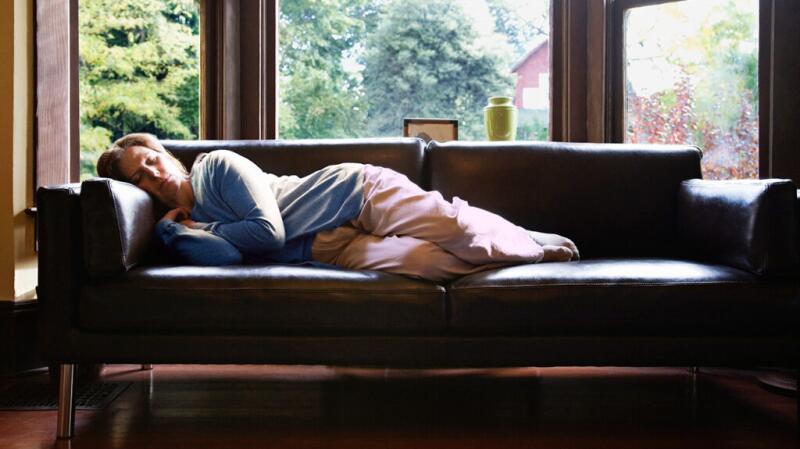 A person lies on a couch and sleeps in the daylight.