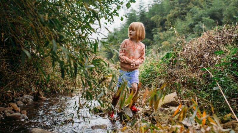 Young girl walking in wooded area with creek