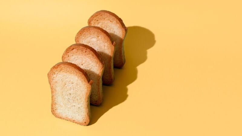 Image of four slices of bread standing upright on yellow surface casting a shadow