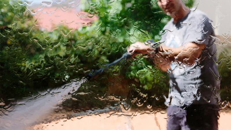 Older man spraying hose toward camera to create blurred effect