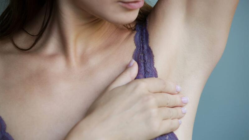 A woman is checking her armpit for lumps.