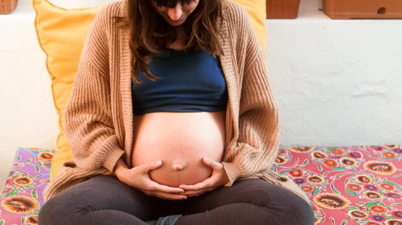 Pregnant person holding bare belly late in pregnancy
