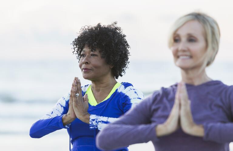 Two mature women exercising on beach, doing yoga