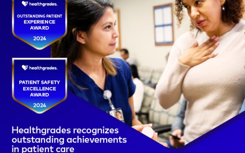A young woman in scrubs listens to a middle-aged patient in a hospital lobby. Below the photo, white text against a dark blue background reads: "Healthgrades recognizes outstanding achievements in patient care."