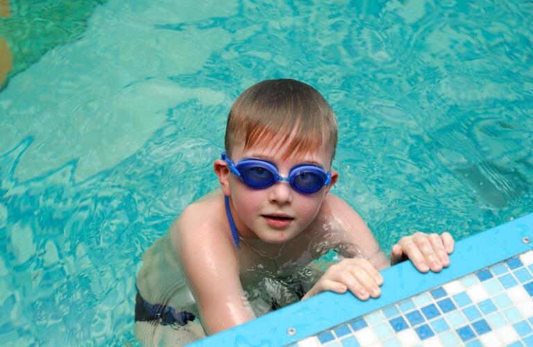 young boy swimming in pool with goggles on