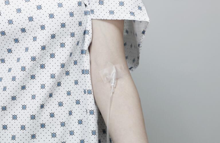 Cropped image of Caucasian woman in hospital gown with IV in arm